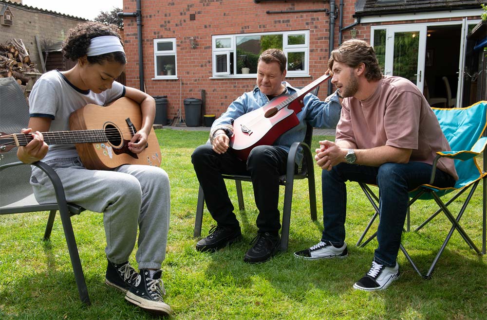 Foster child sat in a garden with their foster family learning how to play the guitar.