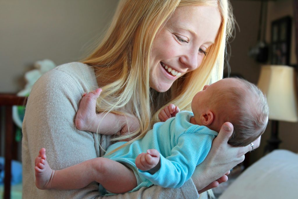 A happy woman holding a baby in her hands and smiling down 