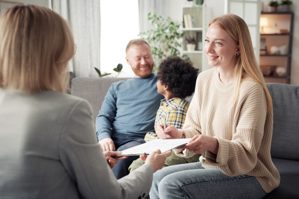 Young woman finding out about becoming a foster carer with man and child in the background.