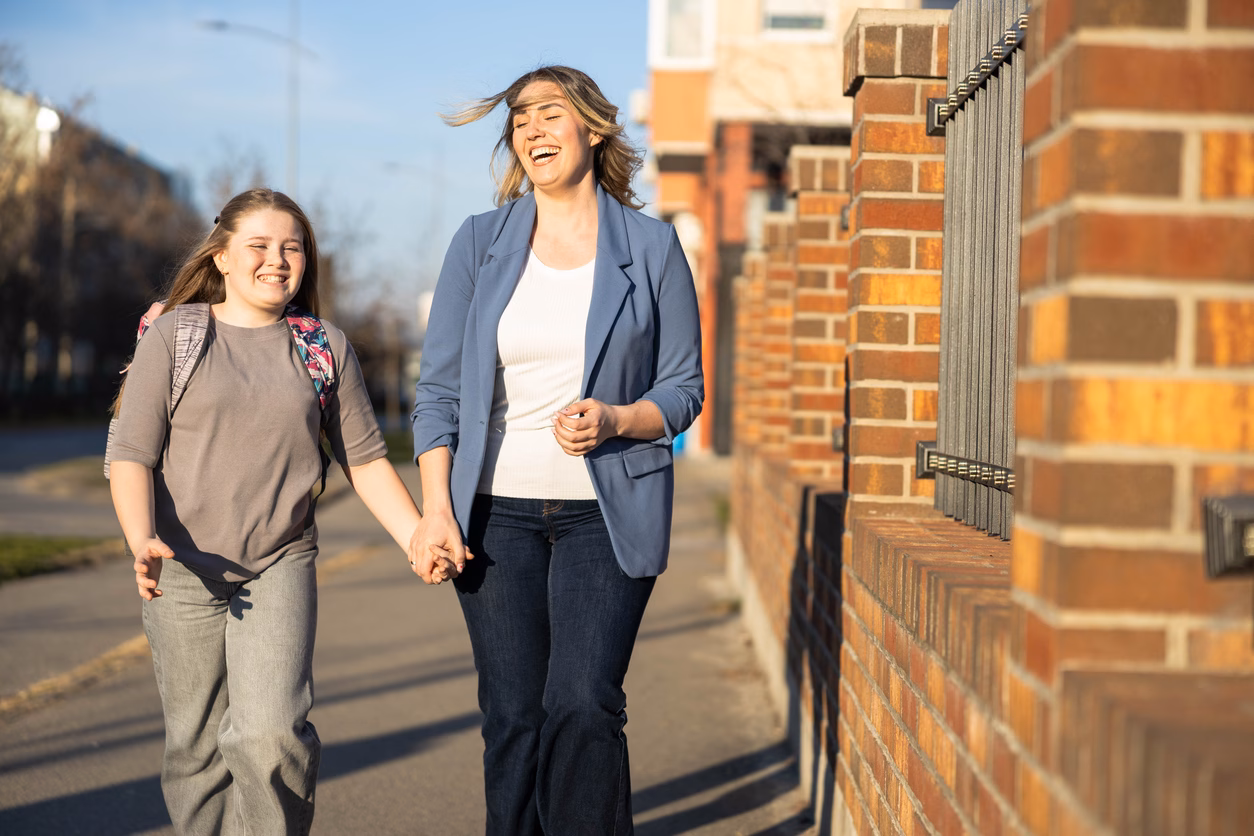 A woman and girl share laughter while walking hand in hand down a pavement